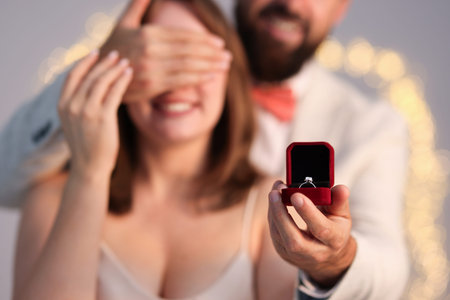 Man with engagement ring making marriage proposal to his girlfriend on light grey background with...