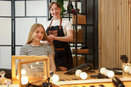 Professional hairstylist combing woman's hair in salonの写真素材