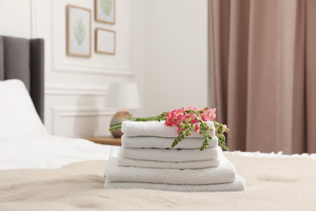 Stack of white terry towels and beautiful flowers on bed indoorsの写真素材