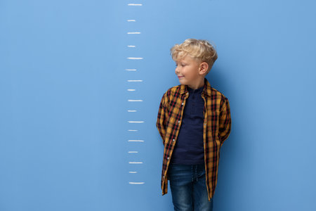 Cute little boy measuring his height near blue wallの写真素材