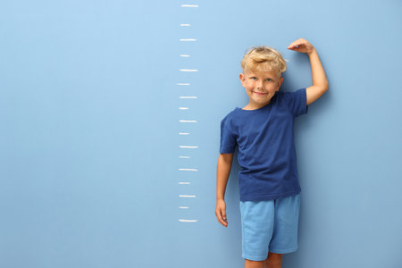 Cute little boy measuring his height near blue wall. Space for textの写真素材
