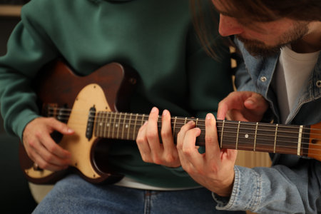 Tutor teaching man to play guitar at home, closeup