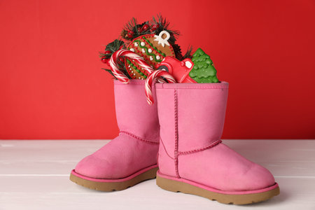 Boots with treats and festive decor on white wooden table against red background