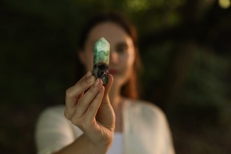 Woman meditating with crystal to heal or restore her aura outdoors, selective focus