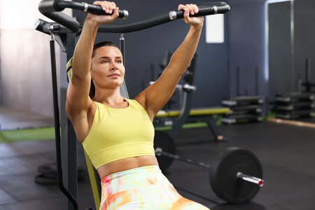 Athletic woman training on shoulder press machine in gym