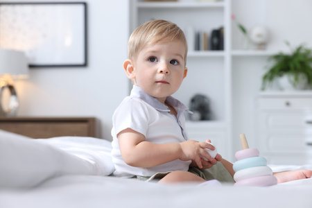 Cute little baby playing with toy pyramid on bed at home