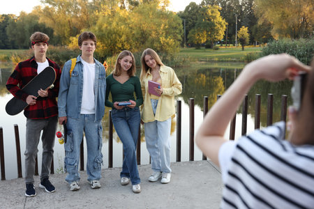 Teenage girl taking photo of her friends near lake outdoors