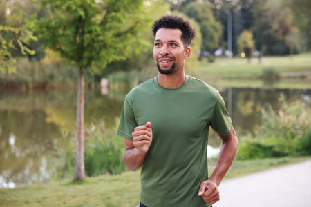 Smiling man running near river outdoors. Healthy lifestyle