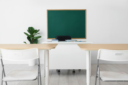 Blank green chalkboard, desks, chairs and plant in classroomの写真素材