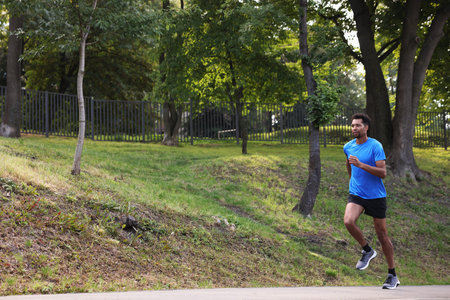 Handsome man in sportswear running in park. Space for text