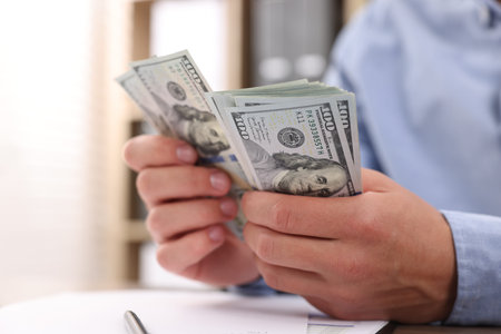 Man counting dollar banknotes at table, closeup