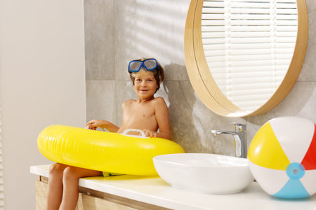 Dreaming about vacation at sea. Little boy with diving mask and inflatable ring in bathroom