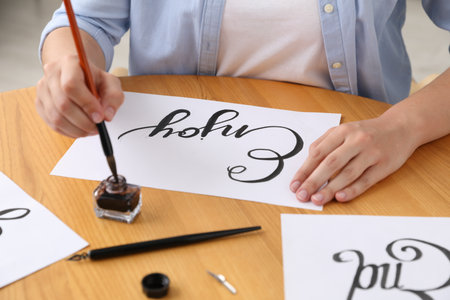 Calligraphy. Woman dipping brush into inkwell at wooden table indoors, closeupの写真素材