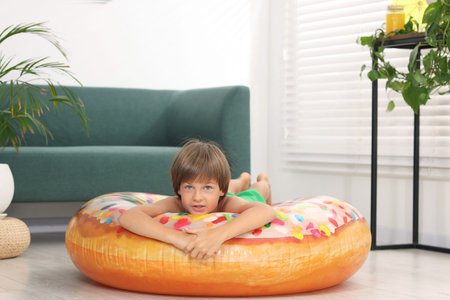 Dreaming about vacation at sea. Little boy on inflatable ring indoors