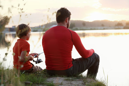 Father and his little son fishing together near river outdoors, back viewの写真素材