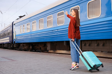 Goodbye. Happy woman with luggage waving near train outdoors