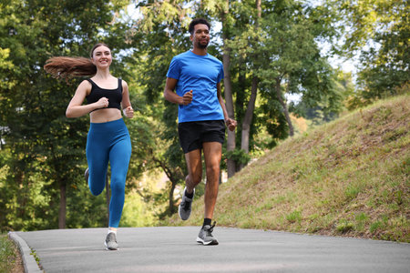 Couple in sportswear running in park, low angle view. Space for text