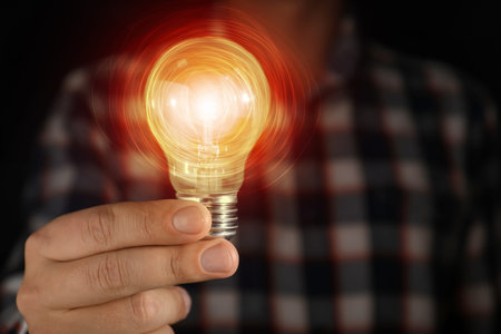 Man holding glowing light bulb in darkness, closeup. Idea concept