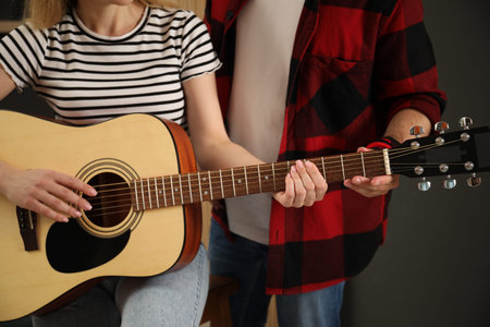 Tutor teaching woman to play guitar at home, closeup