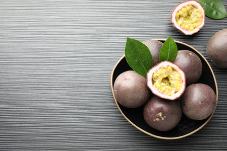Fresh passion fruits with green leaves on black wooden table, above view. Space for text