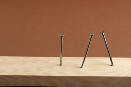 Metal nails in wooden plank on brown background, closeup.の写真素材