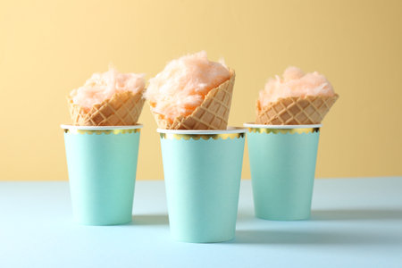 Ice cream cones with cotton candy in paper cups on color background