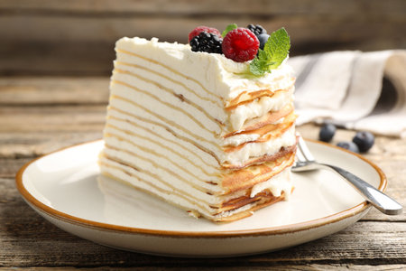 Piece of tasty crepe cake with berries served on wooden table, closeup