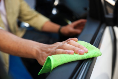 Man wiping car door with green microfiber rag in salon, closeup