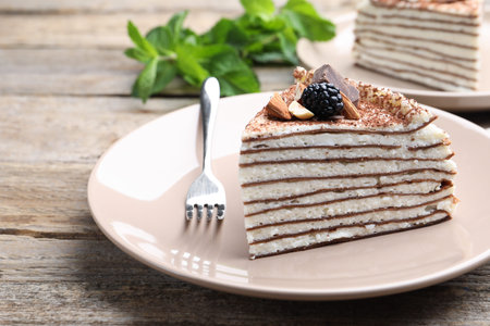 Piece of tasty crepe cake with cocoa powder, chocolate, nuts and blackberry served on wooden table,...