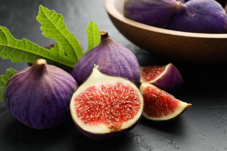 Fresh ripe figs and green leaf on black textured table, closeup