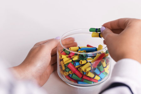 Woman with glass jar of colorful paper pieces at white table, closeup