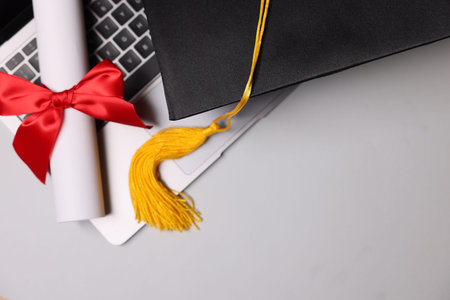 Graduation cap, laptop and diploma on light table, flat lay. Space for text