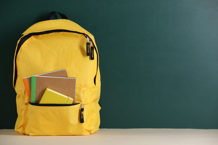 Yellow backpack with notebooks on table near blackboard. Space for text