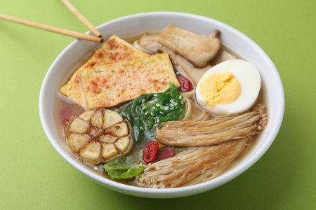 Tasty ramen with enoki and king oyster (eryngii) mushrooms on green background, closeup