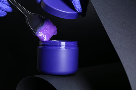 Woman taking hair care product with brush on black background, closeup