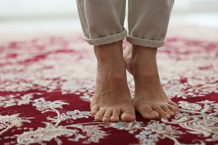 Woman barefoot on red carpet with pattern at home, closeup