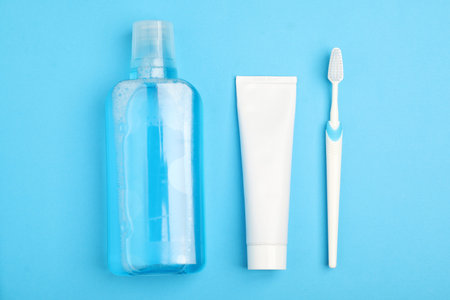 Mouthwash, toothbrush and toothpaste on light blue background, flat lay