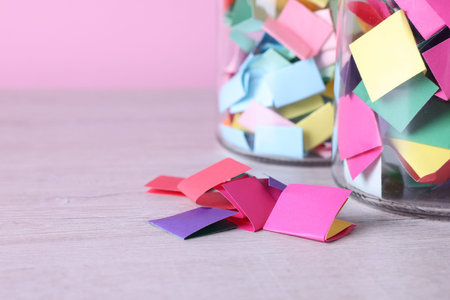 Message notes. Colorful paper pieces in glass jars on wooden table, closeup. Space for text