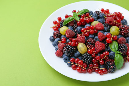Different ripe juicy berries on plate against green background, closeup. Space for textの写真素材