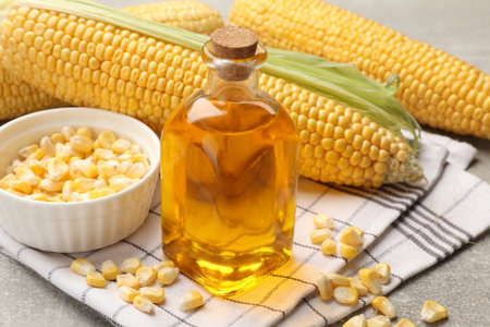 Corn oil in glass bottle, kernels and cobs on gray table, closeupの写真素材