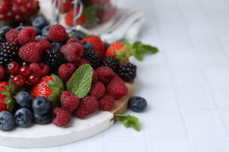 Different ripe berries and mint leaves on white tiled table, closeup. Space for text