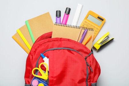 Red backpack with different stationery on light background, flat lay