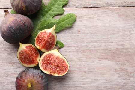 Fresh ripe figs and green leaf on wooden table, flat lay. Space for text