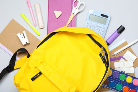 Yellow school backpack with different stationery on gray background, flat lay