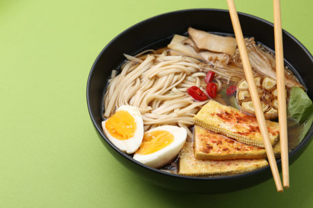 Tasty ramen with enoki and king oyster (eryngii) mushrooms in bowl on green table, closeup