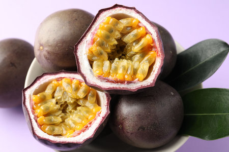 Fresh passion fruits with green leaves on violet background, closeup