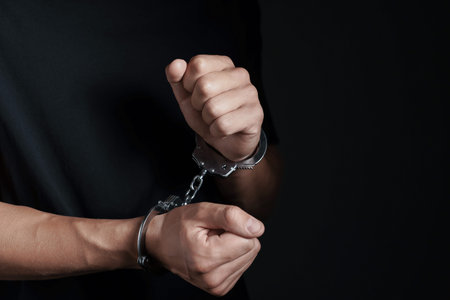 Man in metal handcuffs on black background, closeup. Space for text