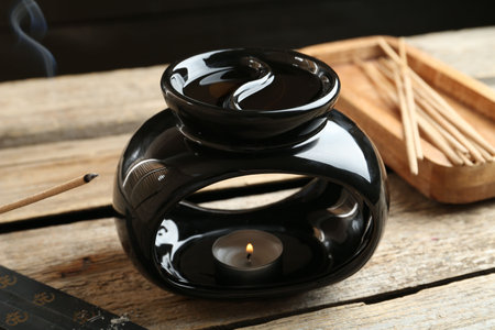 Aroma lamp with burning candle and smoldering incense stick on wooden table against dark background, closeupの写真素材