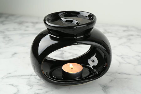Aroma lamp with burning candle on white marble table, closeup