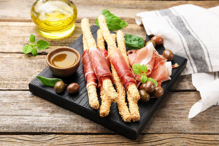 Grissini breadsticks with prosciutto, olives and honey on wooden table, closeup